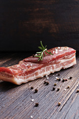 Smoked bacon with rosemary and pepper on rustic woodwn background.