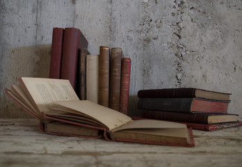 libri antichi appoggiati e aperti su tavolo di legno e muro grezzo © benedetta