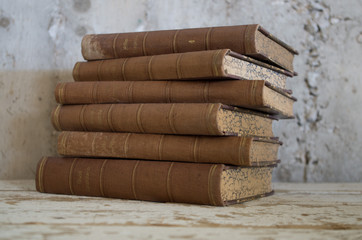 pila libri antichi appoggiati su tavolo legno e con sfondo muro grezzo