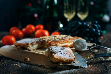 a festive New Year's table, cheese cake with chocolate, tangerines, grapes, biscuits, champagne and two glasses against the backdrop of a decorated Christmas tree with lights