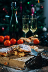a festive New Year's table, cheese cake with chocolate, tangerines, grapes, biscuits, champagne and two glasses against the backdrop of a decorated Christmas tree with lights