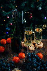 Fototapeta na wymiar a festive New Year's table, cheese cake with chocolate, tangerines, grapes, biscuits, champagne and two glasses against the backdrop of a decorated Christmas tree with lights