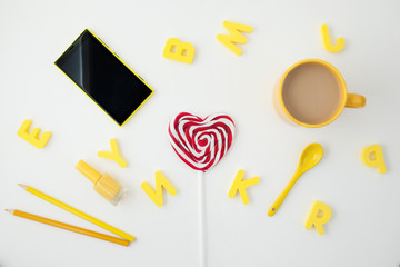 yellow cup, heart shaped candy, letters ,yellow phone and pencils on white background. Place for text. View from above