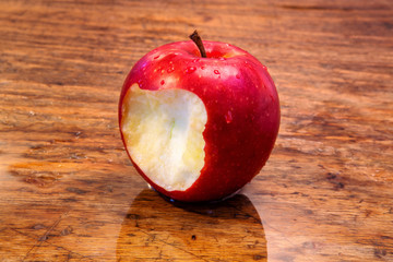 red wet apple with a bite on rustic wooden table