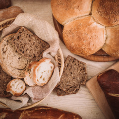 Many mixed baked breads and rolls on rustic wooden table
