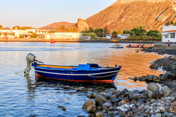 Empty colorful small blue fishing boat with outboard motor anchoring near Stromboli island, Aeolian Islands, Italy