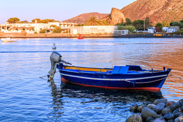 Seagull sitting on outboard motor of colorful small blue fishing boat anchoring near Stromboli...