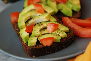 Vegetarian healthy wholegrain bread with avocado and cherry tomatoes on gray plate woth orange napkin
