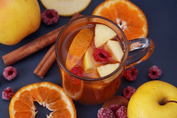 Herbal tea with apple, ginger, lemon, cinnamon and thyme in a glass. Warming tea, healthy fruit infused tea. Horizontal closeup view on blue background