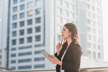 Fototapeta premium Professional young business woman thinking and using mobile digital tablet to accounting at the city in morning. Business woman concept