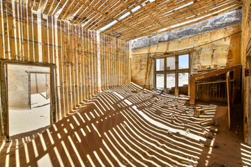 Fototapeta premium Inside view of one of the abandoned houses in the ghost town of Kolmanskop near Lüderitz in Namibia, Africa. After the diamond rush ended, the houses are slowly getting swallowed by sand and dunes.