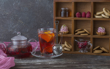 on a wooden table tea in a kettle, a mug with tea and sweets: cookies, cakes, berries, honey