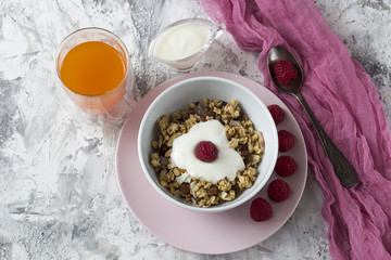 Breakfast muesli with nuts, dried fruits, fresh raspberries and orange juice, yogurt on the table