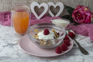 Breakfast muesli with nuts, fresh raspberries and orange juice, yogurt on the table. Decor in the form of heart and peony flower