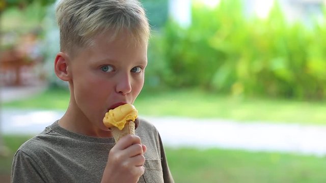 Closeup view of white cute little kid eating mixed ice cream at summer outdoors green grass background.