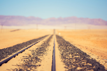 Close up detail view of train tracks leading through the desert near the city of Luderitz in Namibia, Africa. Photo cross processed. Selective focus on foreground. Mountain range in the background.