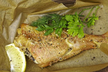 Fried fish trout, lemon and greens on paper kraft background
