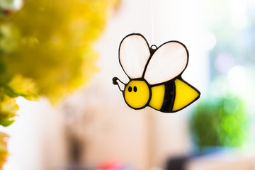 Bee glass ornament hanging from a thread approaching an artifical yellow flower