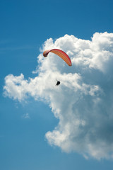 Alone paraglider flying in the blue sky against the background of clouds. Paragliding in the sky on a sunny day.