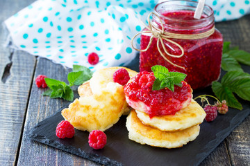 Cottage cheese fritters, pancakes with raspberry jam and fresh raspberries on a wooden rustic table. Copy space for your text.