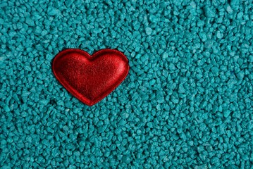 маленькое красное сердце лежит на мелких синих камнях