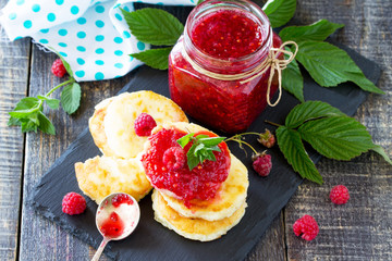 Cottage cheese fritters, pancakes with raspberry jam and fresh raspberries on a wooden rustic table. Background breakfast.
