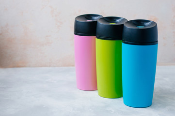 Three plastic color thermos mugs on grey background with copy space