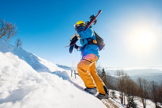 Professional skier walking up the snowy hill in the mountains carrying his equipment on a sunny day copyspace active lifestyle sportsman seasonal recreation downhill activity
