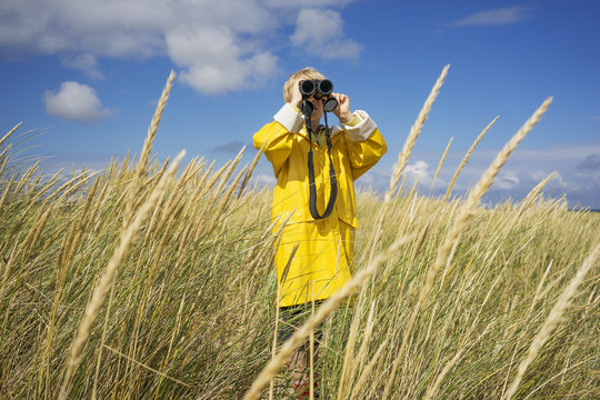 A young boy in wet weather gear looking through binoculars