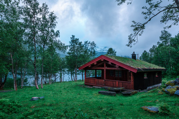 Typical norwegian old wooden houses with grass roofs near forest lake, Norway.
