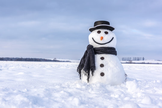 Funny snowman in stylish hat and black scalf on snowy field. Merry Christmass and happy New Year!