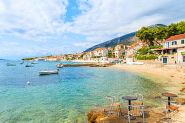 Metal cafe chairs on beach in Bol port with typical town architecture, Brac island, Croatia