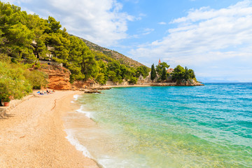 Beach with emerald green sea water and view of Dominican monastery in distance, Bol town, Brac island, Croatia