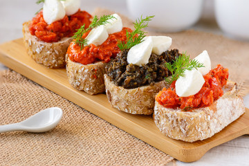 Appetizer bruschetta with mozzarella cheese, pepper-tomato paste, dried tomato paste with garlic and basil and  black olives paste with marinated capers.