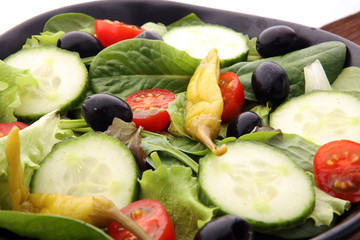 bowl of salad with vegetables and greens, with tomato, cucumber and onions.