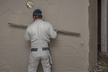 Plasterer concrete worker processes the applied gypsum plaster at wall of house construction at...