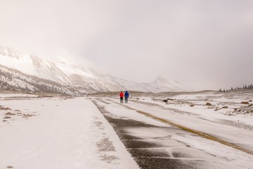 Two people in colorful coats walking down a frozen snow covered road to a mountain - Canadian Rockies winter