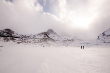 Two people in colorful coats walking down a frozen snow covered road to a mountain - Canadian Rockies winter