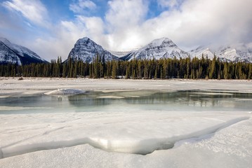 A frozen river with a snowy mountain back drop on a beautiful winter day - Canadian Rockies