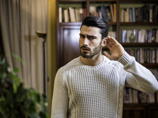 Handsome young man can't hear, putting hand around his ear. Indoors shot inside a house