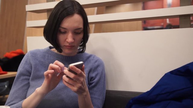 Portrait of young woman using smartphone sitting in cafe.