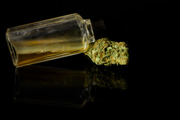 Medical Oil Cannabis - stick resin, apothecary bootle with oil and marijuana flowers on the black mirror background.