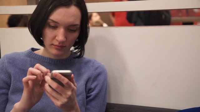 Young cute girl using smartphone sitting in cafe.
