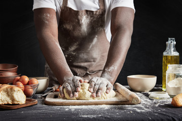 Cropped shot of talented dark skinned male cook kneads studiously dough, prepares for culinary competiton, isolated over black chalk background. African American male bakes something delicious