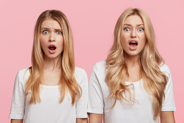 Emotional blonde young females with shocked and angry expression keep mouthes opened, being amazed to realize about loosing important beauty competition, isolated over pink studio background