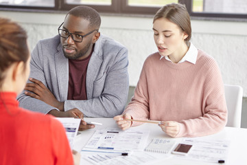 Group of mixed race employees search information for startup, do paper work, communicate during brainstroming session. Professional young skilled traders make business plan together, collaborate