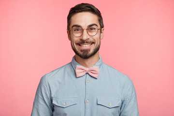 Portrait of happy smiling unshaven man dressed in festive clothes and round spectacles, happy to be...