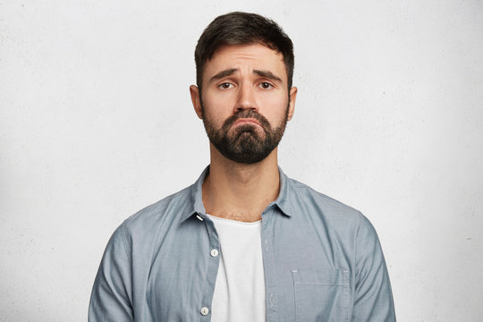 Horizontal shot of attractive male model with unhappy expression curves lips as feels frustration, being upset to hear bad news, isolated over white background. Negative human facial expressions