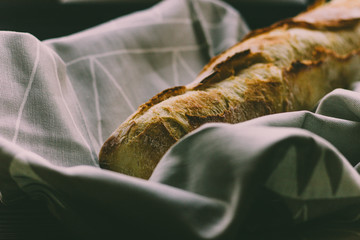 Fresh bread french baguette on a cloth and black wood, moody dark food photography