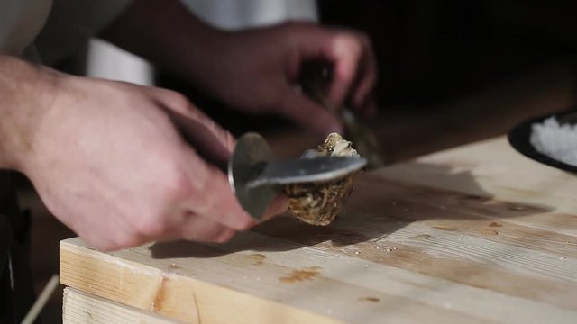 Chef in a luxury fish restaurant opens oysters on the table and puts them on a plate with ice